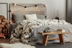 Wooden bench in the foot of the bed with grey bedding and cozy blanket